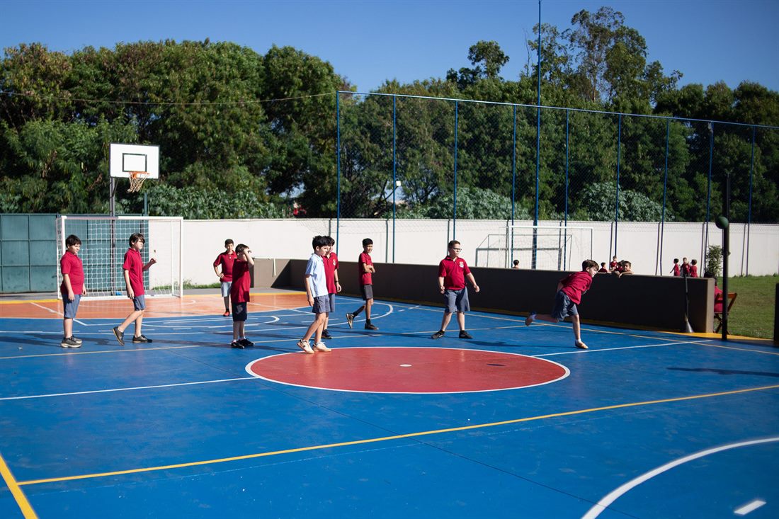 Alunos jogando basquete na quadra coberta